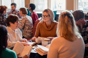 Groupe de personnes entrain de discuter autour d'une table, livres à la main